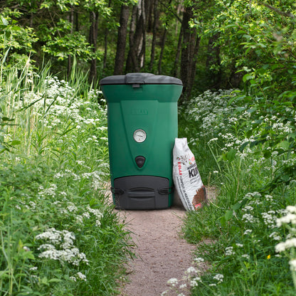 Green compost bin with a bag of compost on a forest path