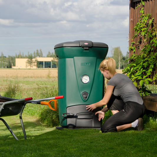 Person interacting with a green compost bin in an outdoor setting